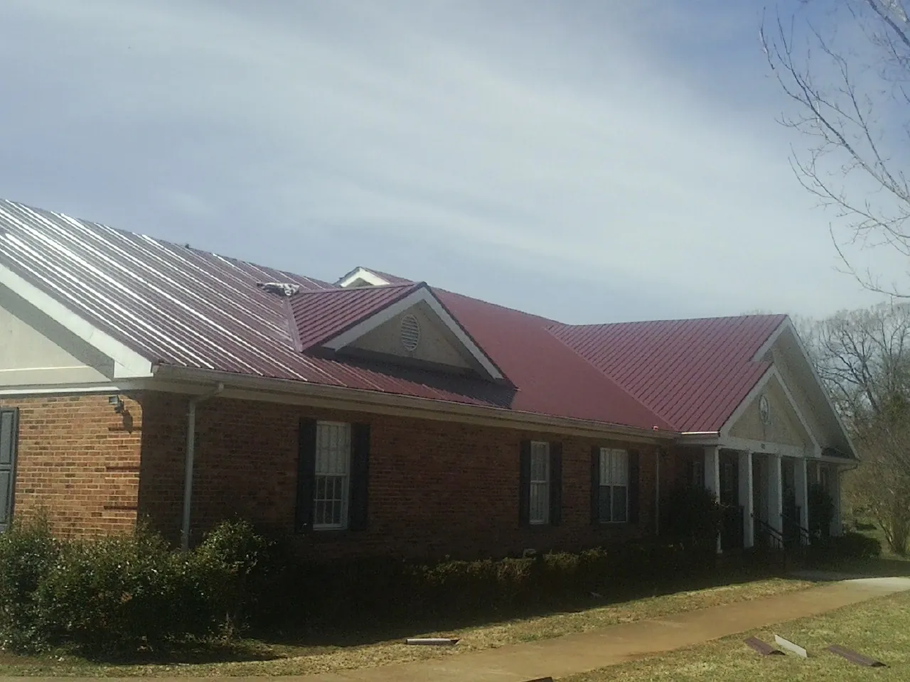 Red metal roof with gabled entries on a long brick building, from a Hail Damage Roof Repair job in Davisburg