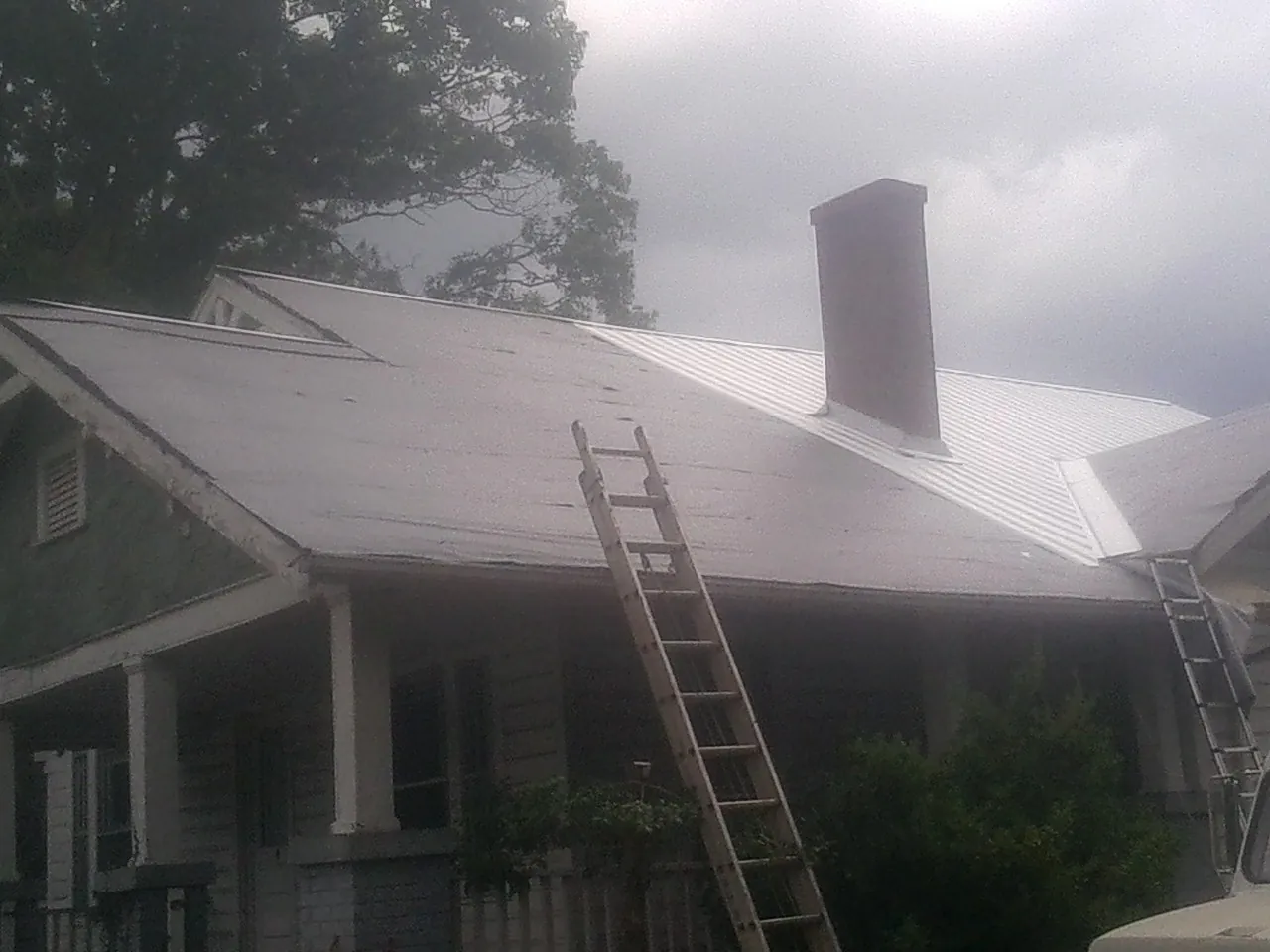 Ladders against a metal roof on an older home with a brick chimney in Davisburg