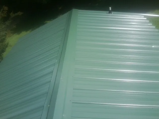 New green metal panels meeting at the ridge of a roof — Flat Roof Repair work by our crew in Davisburg