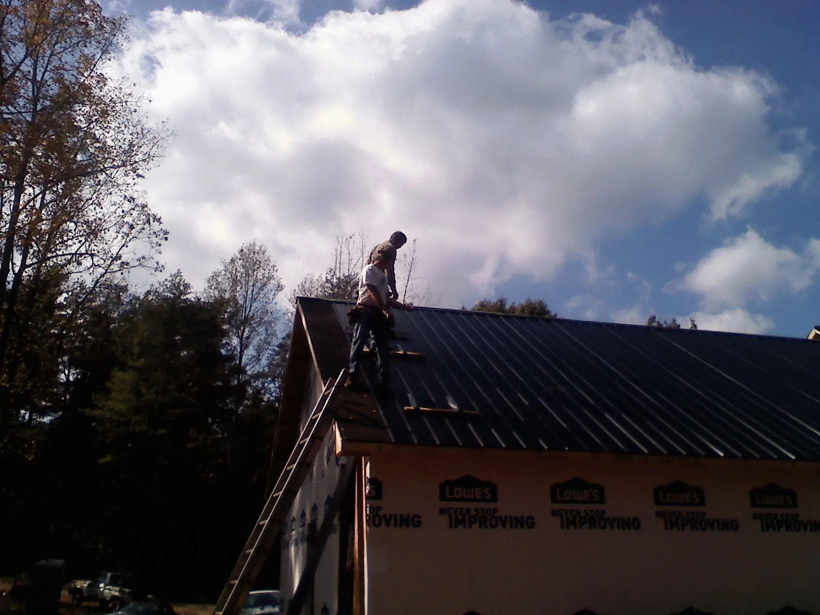 Roofer fastening dark metal panels high against a cloudy sky, from a Roof Inspection job in Davisburg