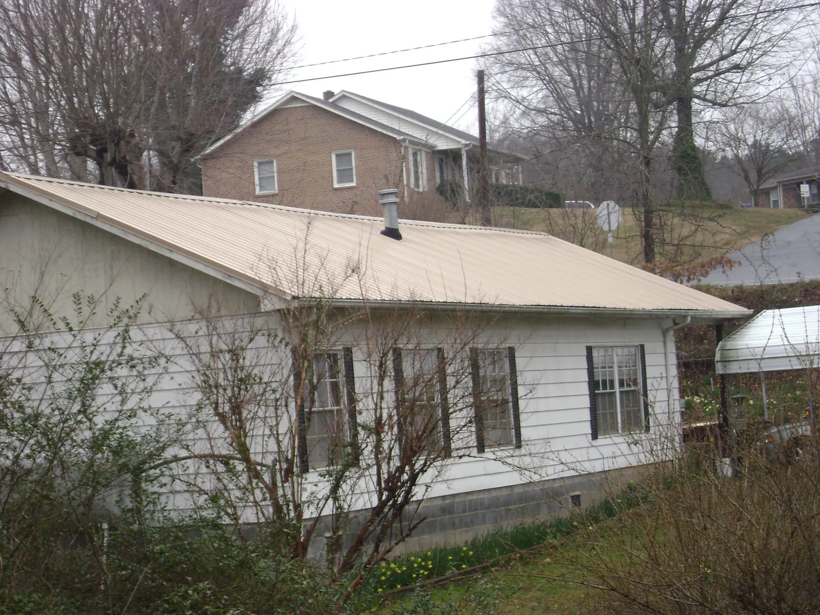 Tan metal roof on a white sided house set into a hillside — Commercial Roofing by Roofing Brothers in Davisburg